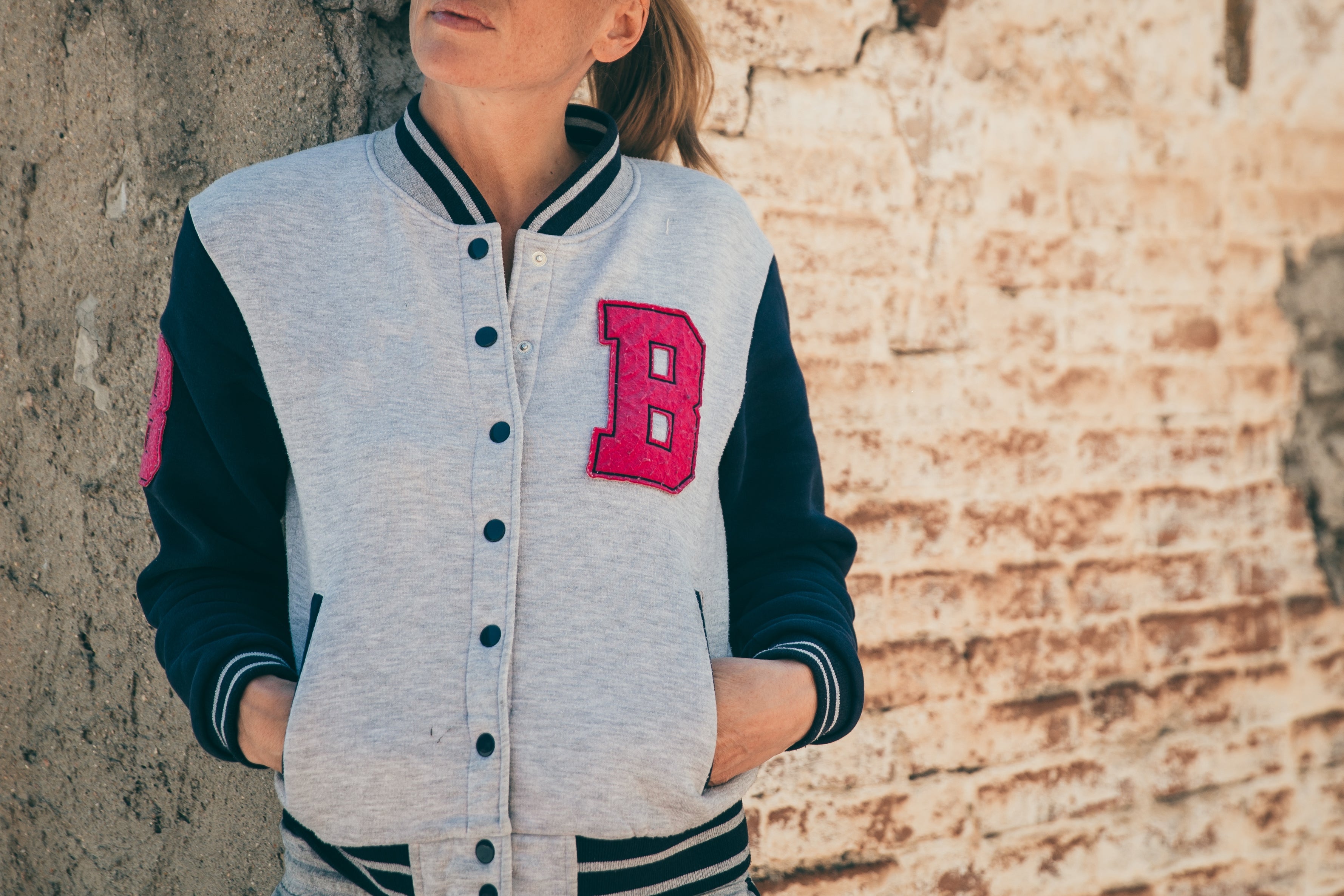 Ragazza appoggiata a muretto con felpa streetwear, con logo B rosa ben visibile lateralmente sul petto