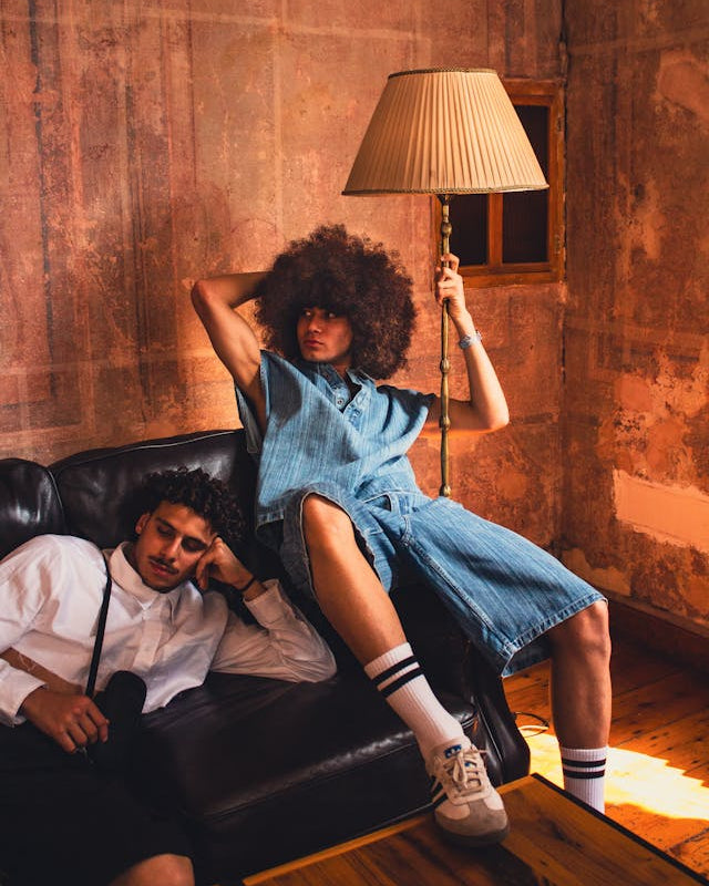 Ragazzo afro in posa su divano, con un ragazzo elegante con camicia bianca di fianco, sempre in posa